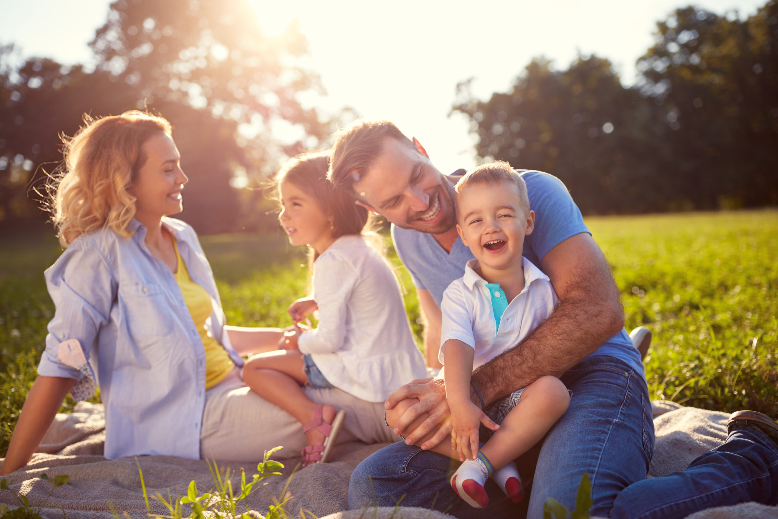 Happy family and their 2 young kids sitting and playing outside
